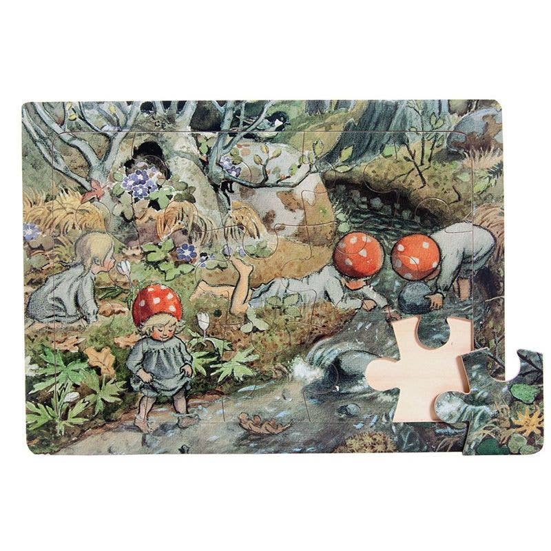 A nearly complete Puzzle - Elsa Beskow "Children of the Forest" Wood Frame Puzzle shows children in red toadstool caps by a forest stream. One piece is missing from the bottom right corner of this charming Scandinavian illustration.