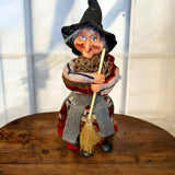 The Marketplace24 Kitchen Witch: Nonna Red, a 10" tall kitchen witch doll with broom, stands on display—a charming piece of Nordic decor and a Scandinavian good luck charm for your home.