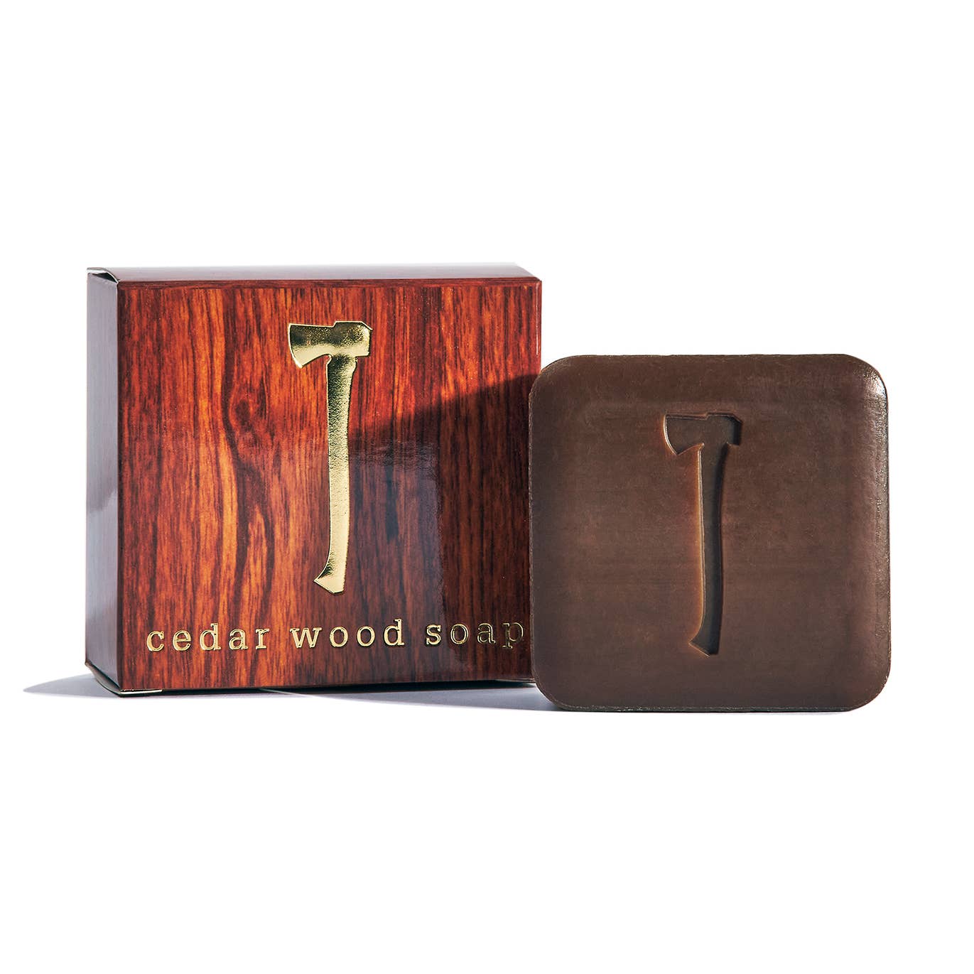 A square, dark brown cedar wood soap bar with an axe imprint appears beside its matching “Soap: Cedar Wood Soap Bar Soap 5.4oz” box, highlighting this vegan soap’s natural cleansing properties.