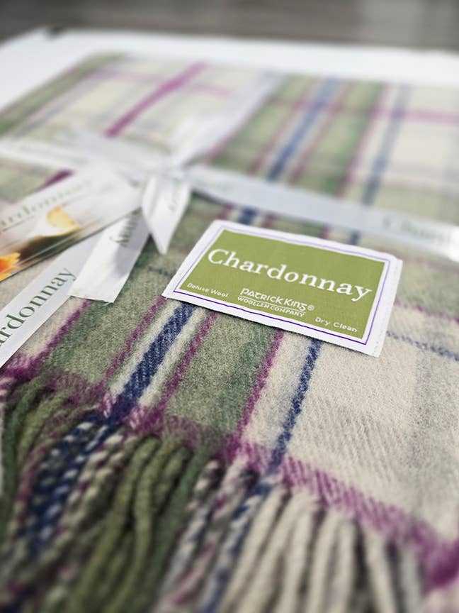 A close-up of the Blanket: Chardonnay Deluxe Tartan Blanket Merino Wool by Patrick King Woollen Company, featuring green, purple, and cream hues—this cozy blanket exudes timeless style and warmth.