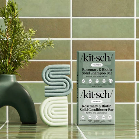 Two boxes of Kitsch Hair: Rosemary & Biotin Volumizing Shampoo & Conditioner Bar Combo (2 bars, 2.7oz each) are displayed with modern soap bars and a rosemary vase on tile—ideal haircare for fine hair.