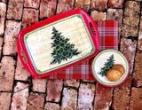 The Merry Christmas Tree Bamboo Serving Tray rests on a plaid cloth; the tray, adorned with festive tree designs and holding cookies, creates a charming hostess gift for Christmas on a brick surface.