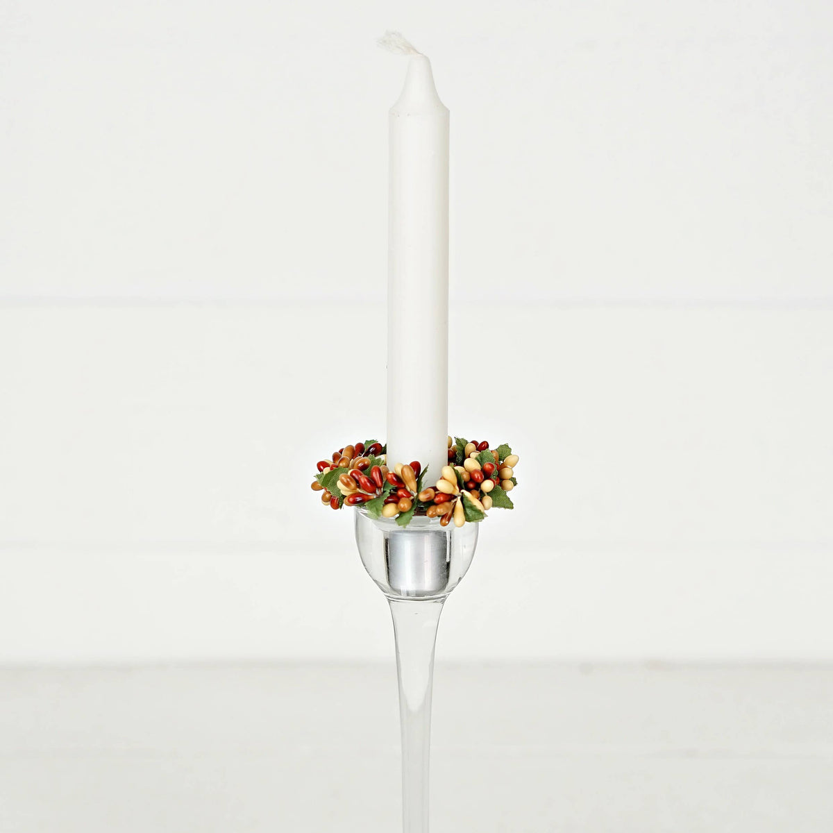 A white taper candle in a tall glass holder, decorated with a pip berry taper ring.