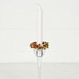 A white taper candle in a tall glass holder, decorated with a pip berry taper ring.