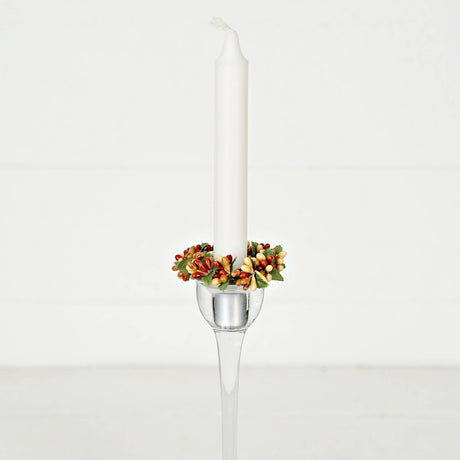 A white taper candle in a tall glass holder, decorated with a pip berry taper ring.