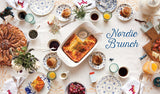 A table set for brunch with pastries, fruit, and drinks evokes cozy Nordic vibes inspired by "Book: Scandinavian Gatherings" (paperback) by Melissa Bahen from Penguin Random House, with the book title displayed on the right side.