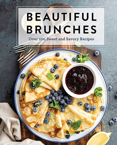 Cookbook cover of "Book: Beautiful Brunches" showcasing folded pancakes topped with blueberries and mint, accompanied by a side of berry sauce, offering delightful recipes for every occasion.