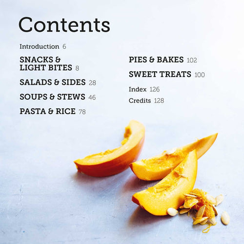 A sliced pumpkin with seeds rests on a light surface next to the table of contents for the book "Pumpkin: 50 Cozy Recipes for Cooking with Pumpkin From Savory to Sweet," which includes sections such as Warming Soups, Snacks & Light Bites, and Pies & Bakes, all dedicated to delightful pumpkin recipes along with their corresponding page numbers.