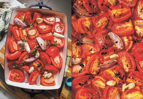 Halved tomatoes, garlic, and shallots with herbs rest in a rectangular baking dish, perfectly prepped for roasting—a delightful beginning for scrumptious soups or other nutritious recipes from the book "Every Season is Soup Season.