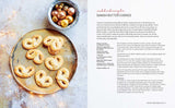 Seven Danish butter cookies with pearl sugar on a gold tray, next to festive ornaments on a white surface.