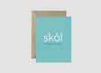 The "Skål Cheers To You!" 4.25x5.5 inch aqua Scandinavian greeting card features white text and comes blank inside with a brown recycled kraft envelope—ideal for congratulations on any occasion.