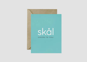 The "Skål Cheers To You!" 4.25x5.5 inch aqua Scandinavian greeting card features white text and comes blank inside with a brown recycled kraft envelope—ideal for congratulations on any occasion.