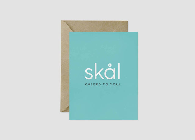 The "Skål Cheers To You!" 4.25x5.5 inch aqua Scandinavian greeting card features white text and comes blank inside with a brown recycled kraft envelope—ideal for congratulations on any occasion.