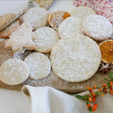 A variety of intricately embossed cookies crafted using the Rolling Pin: Pet Love Embossing Rolling Pin with Cats & Dogs, sprinkled with powdered sugar on a wooden board, surrounded by dried orange slices and berries.