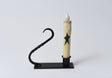 Battery-operated taper candle with a black star design in a black iron candle holder with a twisted handle.