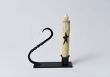 Battery-operated taper candle with a black star design in a black iron candle holder with a twisted handle.
