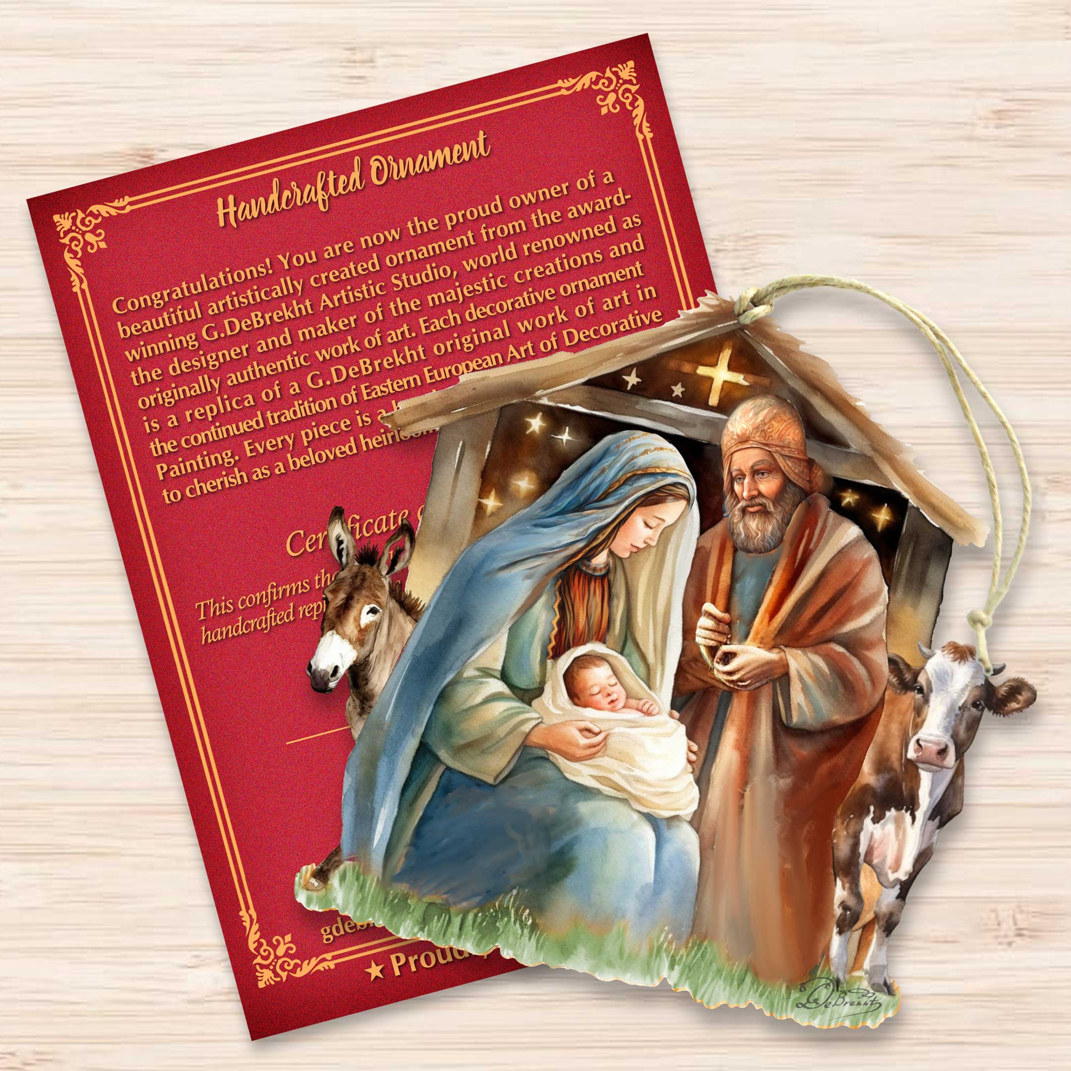 G. DeBre introduces the handcrafted "Born Under Bright Star Nativity" wooden ornament, depicting Mary, Joseph, and baby Jesus in a stable setting. This exceptional Nativity Holiday Décor is showcased alongside a red certificate of authenticity on a wooden table.