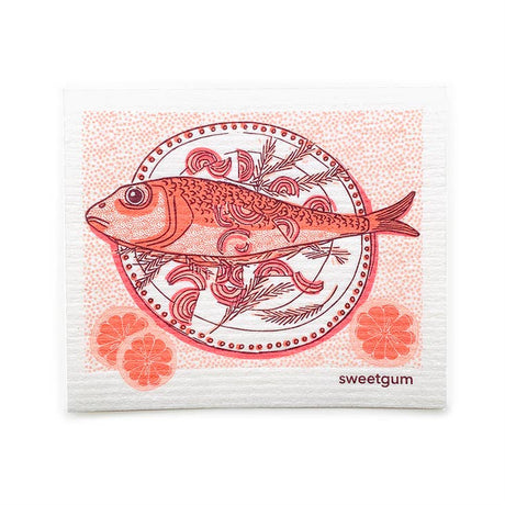 The Dish Cloth: Fish Dinner on a Plate features a fish illustration on a patterned plate with citrus slices, in red and pink hues, plus "sweetgum" printed in the corner—a decorative Swedish-inspired napkin.
