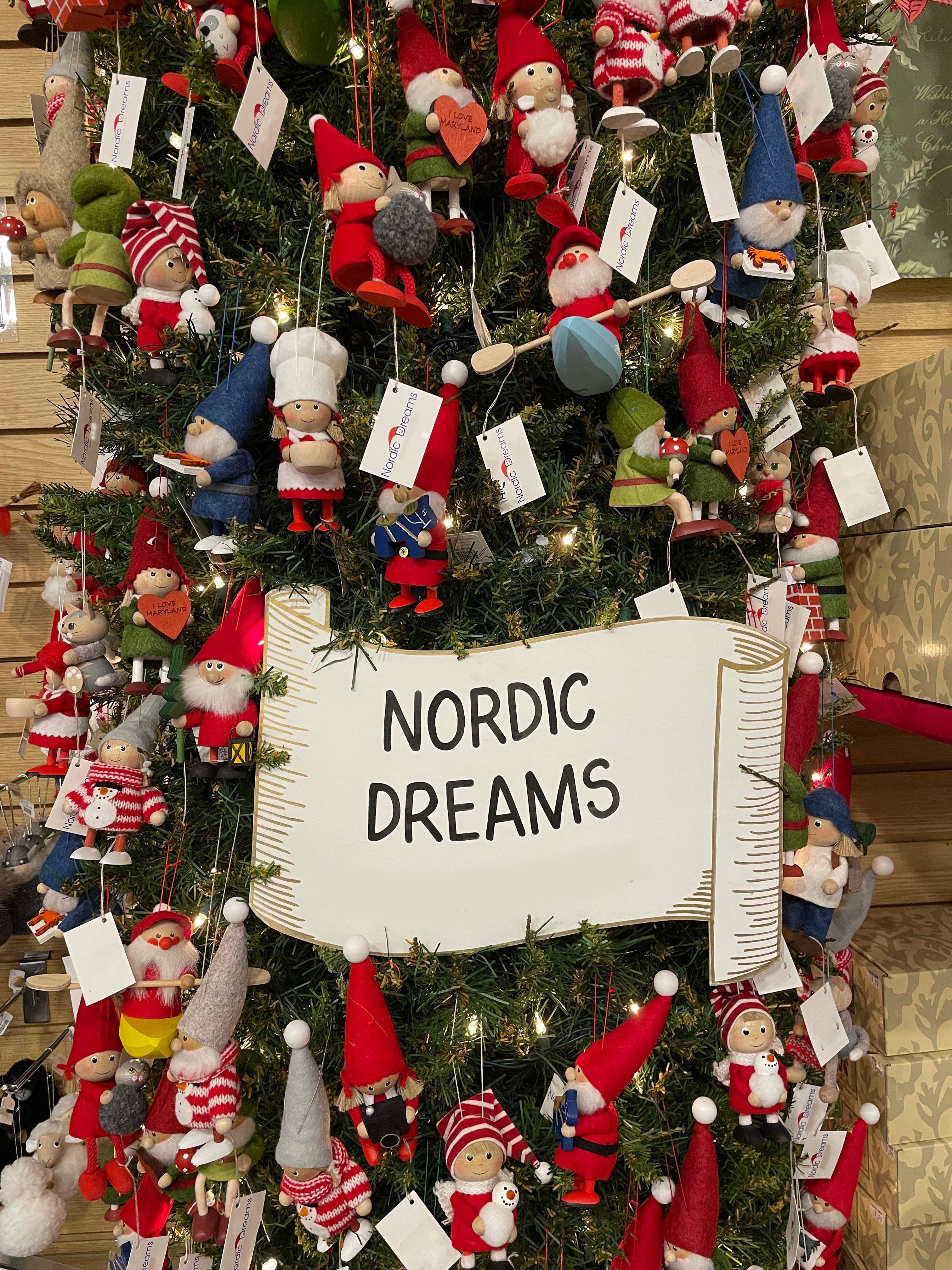 Close-up of a beautifully decorated Christmas tree featuring handcrafted Santa on paddle board ornaments and a charming sign reading "Nordic Dreams.