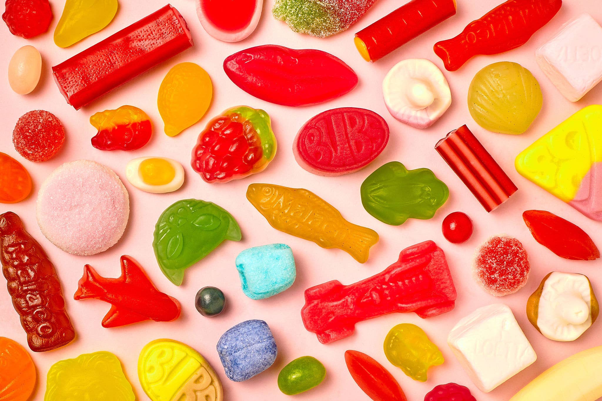 The Candy: Sweet Mix Swedish Gummy Candy Bag 8oz features assorted colorful gummies—fish, cars, fruit, and geometric shapes—on a light pink background. Made with Non-GMO ingredients for a delightful treat.
