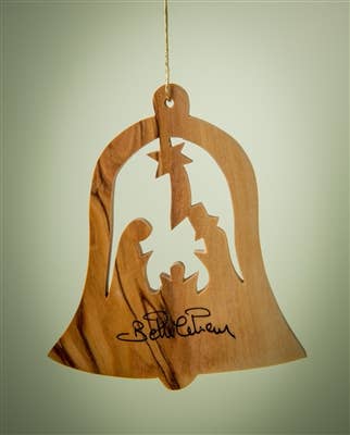 The Ornament: Bell with Nativity - 3" Christmas Tree Ornament is handcrafted in a bell shape with a nativity cutout and signature at the bottom, hanging by a string against a plain background.