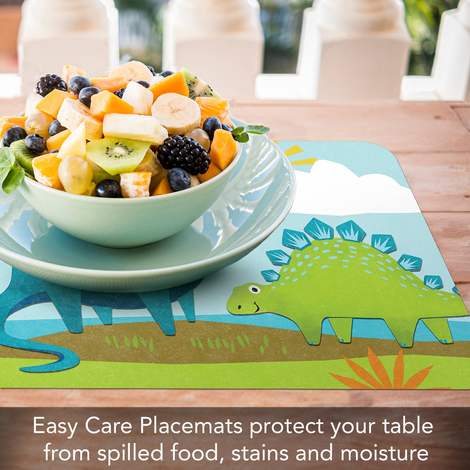 A bowl of fruit salad sits on the Kids Dino World Reversible Rectangular Plastic Placemat, which is BPA-free and dinosaur-themed, on a wooden table.