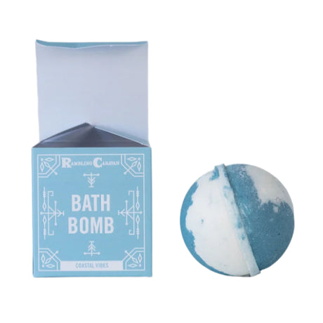 A blue and white, skin-nourishing bath bomb sits beside its light blue box labeled Soap: Coastal Vibes Bath Bomb, handmade by Rambling Caravan in Virginia Beach.