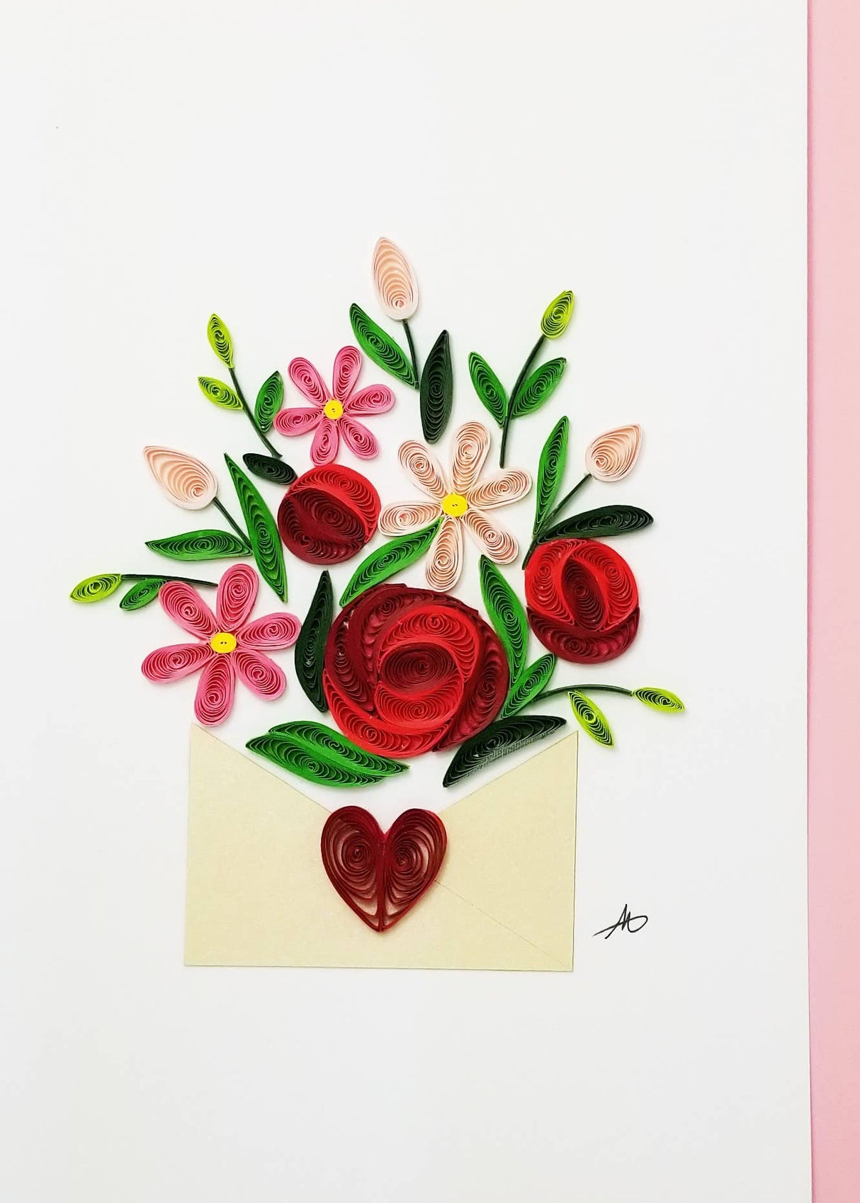 A 5x7 inch blank greeting card featuring a bouquet of red and pink quilled flowers with green leaves in an open envelope with a red heart, set on a white and pink background. Includes a pink envelope.