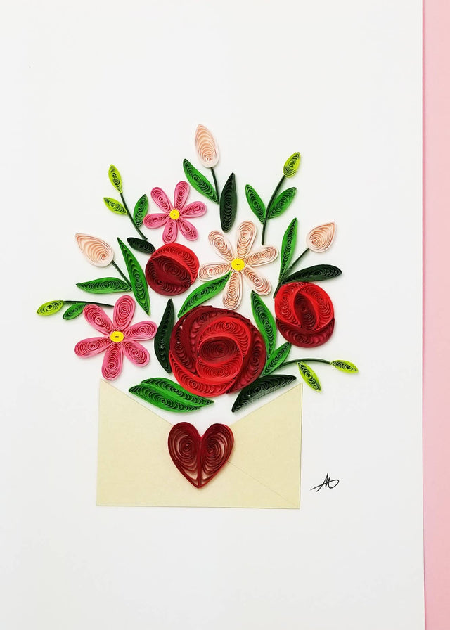 A 5x7 inch blank greeting card featuring a bouquet of red and pink quilled flowers with green leaves in an open envelope with a red heart, set on a white and pink background. Includes a pink envelope.