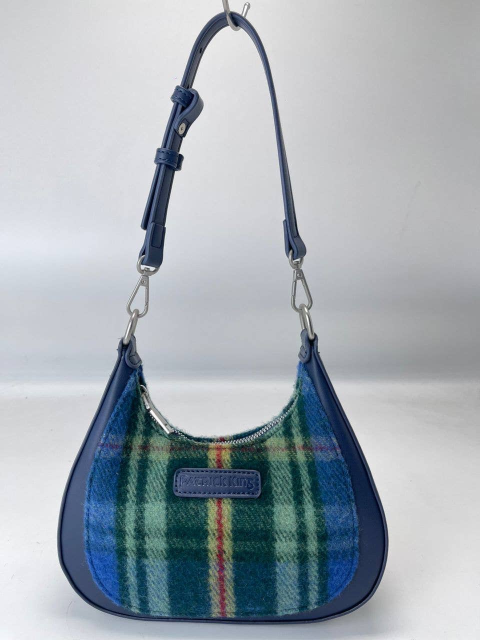 The Bag: Tartan Merino Wool Bag - Nova Scotia is a blue shoulder bag with an adjustable strap, zip closure, and green, blue, yellow, and red tartan wool front panel inspired by the Nova Scotia tartan, plus a stitched brand label.