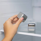 A hand places a Cubes: Stainless Steel Ice Cube (1.57" Square) from the Set of 2 into its plastic case and puts it in the refrigerator.