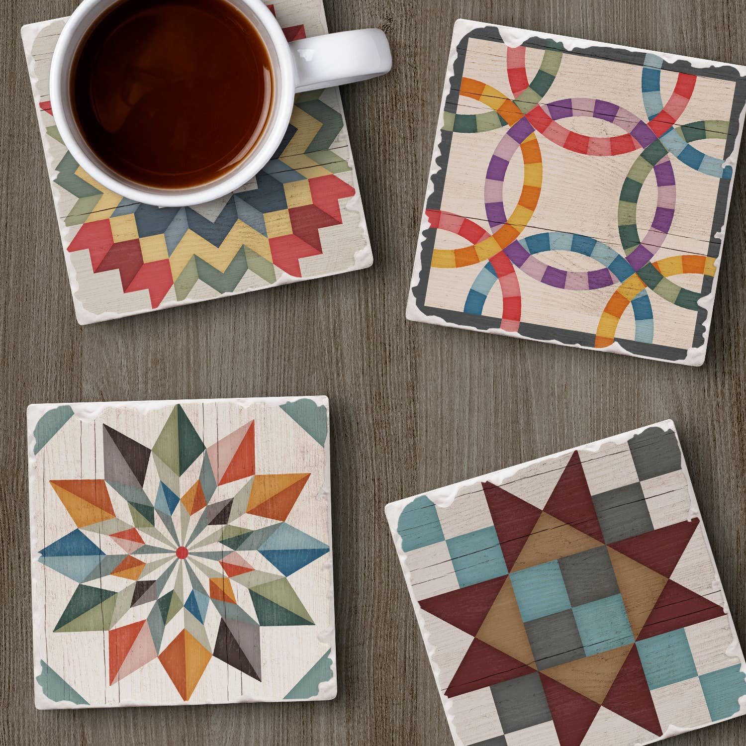 A coffee cup rests on a table with Barn Quilt Signs Stone Coasters, a 4-pack featuring colorful geometric and quilt-inspired patterns. Each coaster has a cork backing to prevent scratches, combining art and function effortlessly.