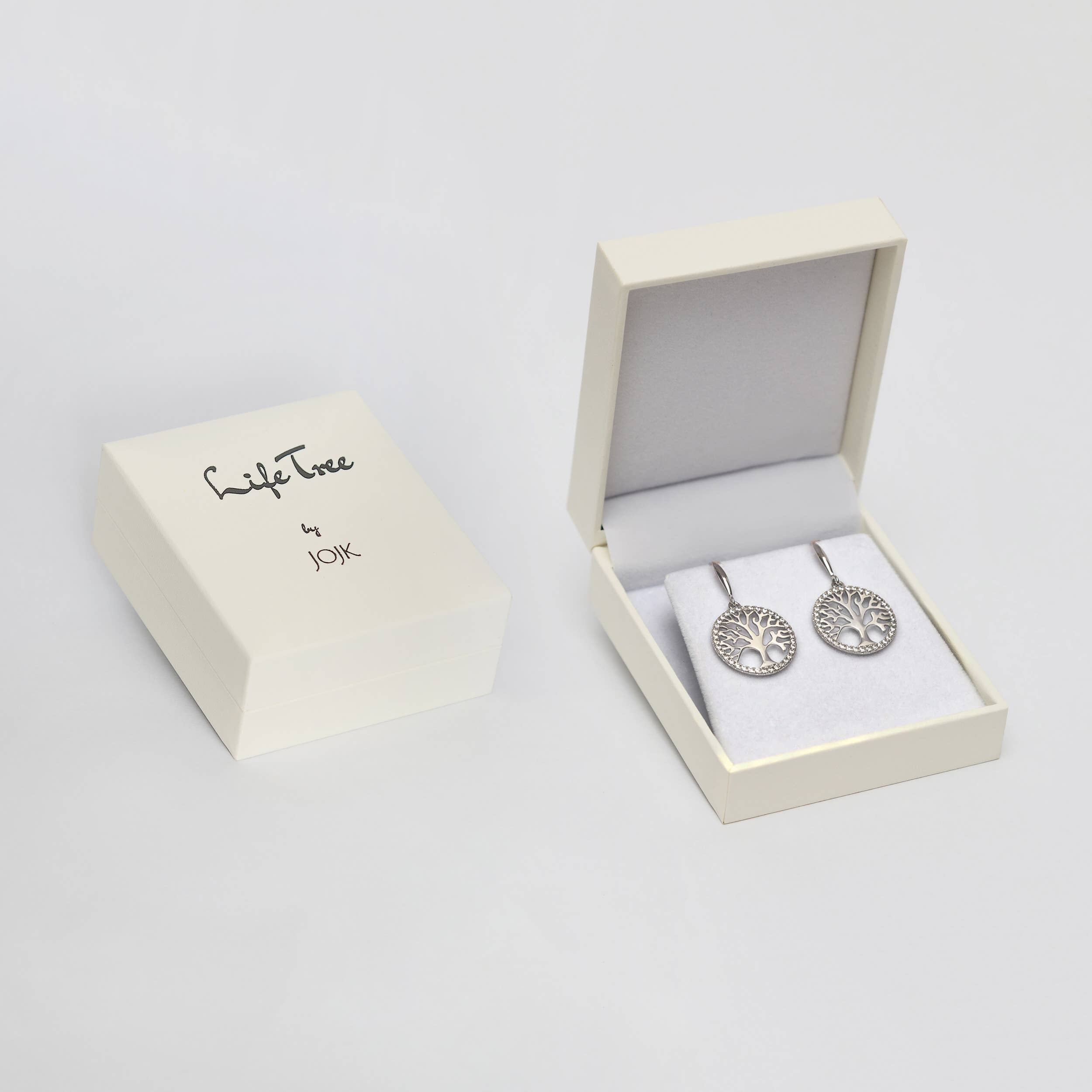 A white JOIK jewelry box rests next to an open box displaying the Earrings: Tree of Life in Sterling Silver with Beautiful Luster on white padding.