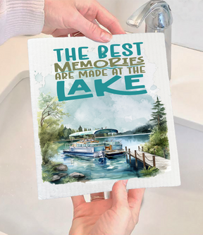 A person holds the "Dish Cloth: Best memories are made at the Lake Swedish Dishcloth" above a sink, featuring boat illustrations and a heartfelt message—an eco-friendly, charming addition to kitchen decor.