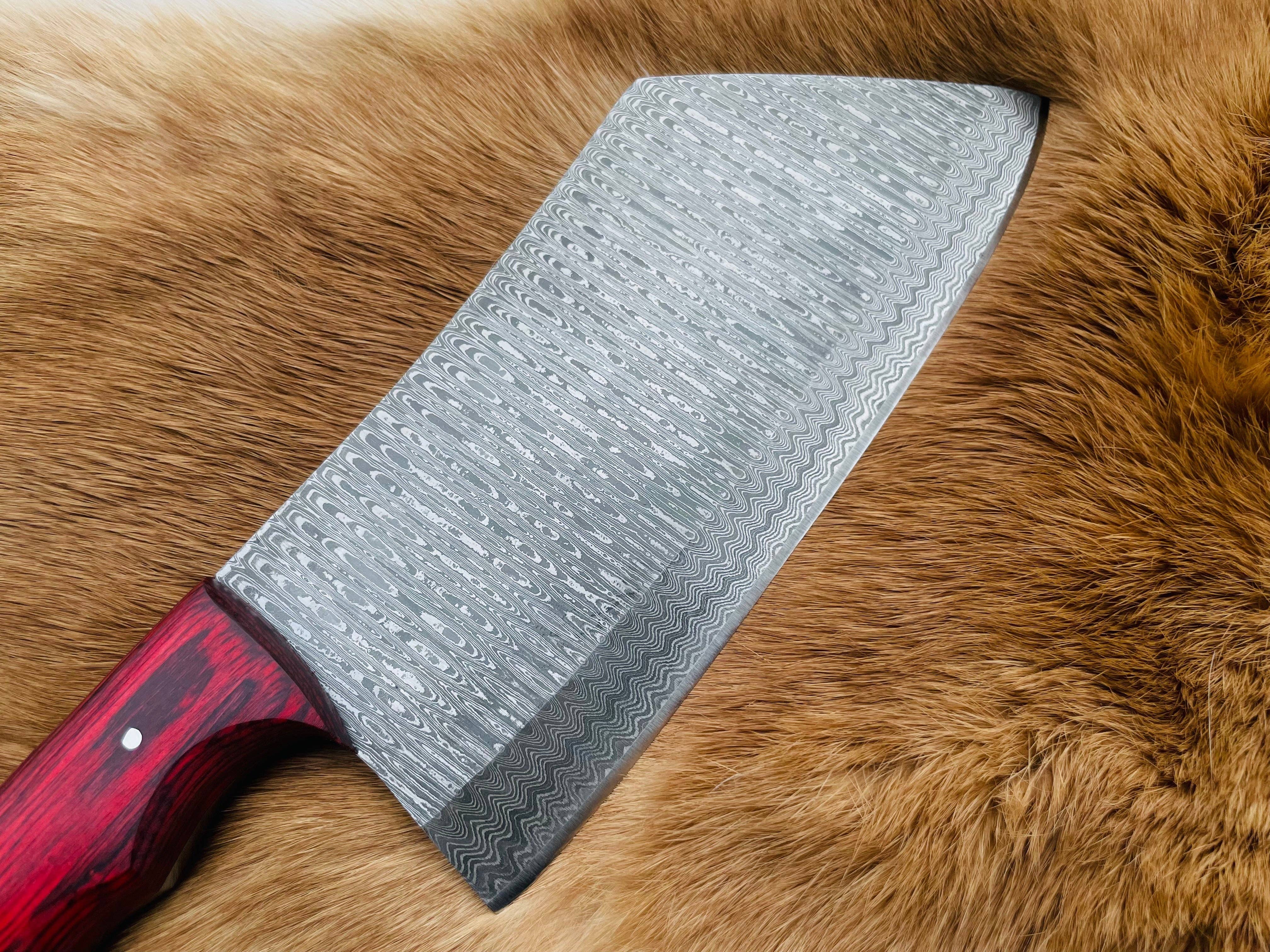 The Knife: Custom Damascus Steel Cleaver Red Handle Chinese Cleaver features an intricate blade pattern and rests on light brown animal fur, its striking red handle and gleaming steel catching the light.