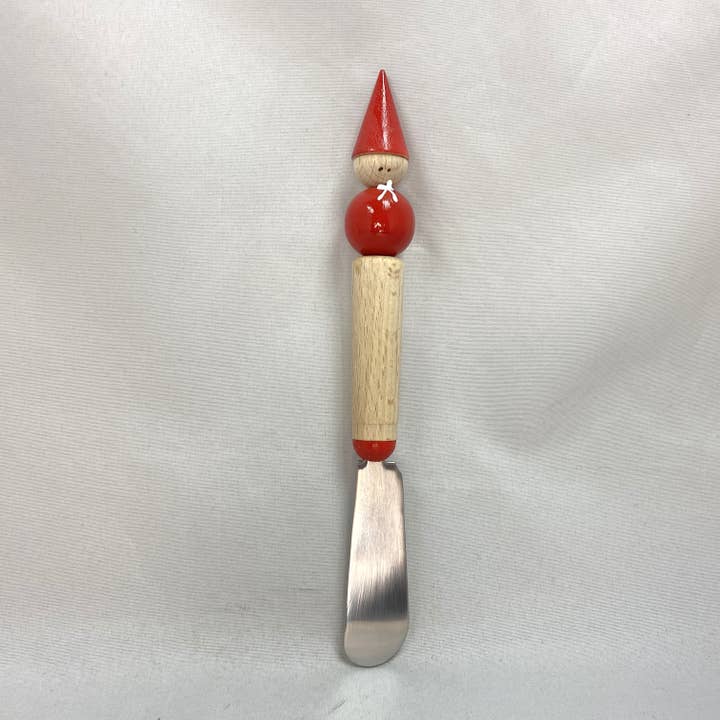 The Spreader: Tomte Finland is a handmade spreader with a wooden handle shaped like a doll. It features a red hat and outfit, capturing the essence of Scandinavian heritage against a plain background.