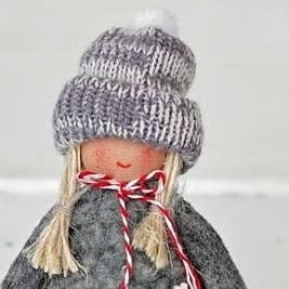 Scandinavian gnome ornament wearing a grey knitted beanie with a white pom-pom and matching sweater, finished with red and white twine tied around the neck.