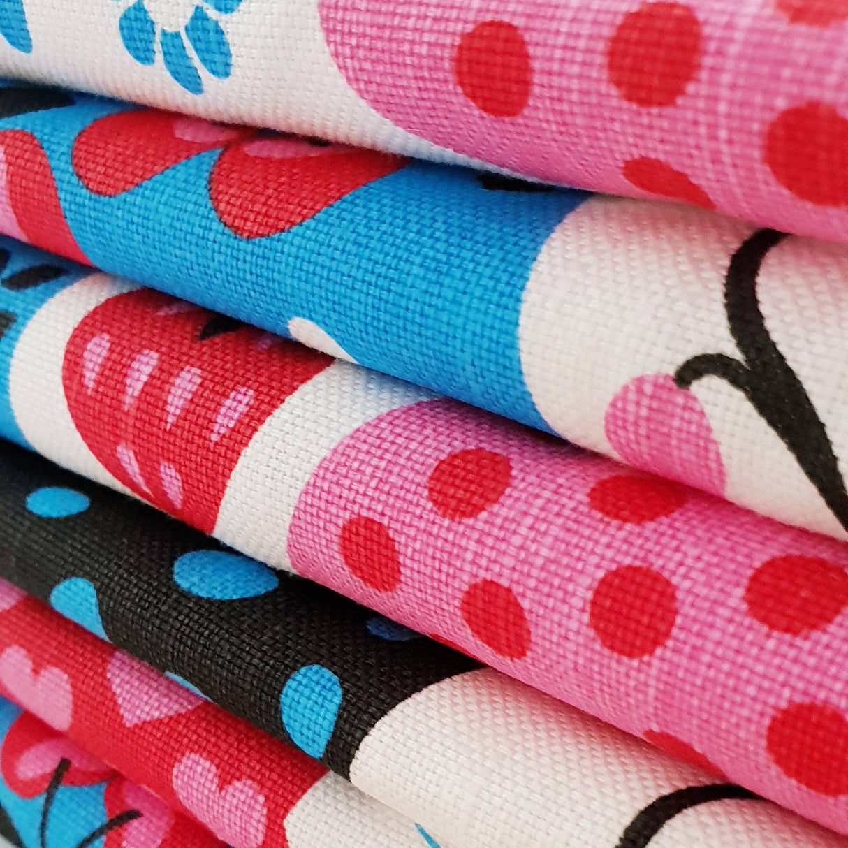 Close-up of stacked folded Tea Towels: Swedish Dala Horse Linen-Cotton Kitchen Towels by Lotta Spjute, featuring colorful patterns in red, pink, blue, black, and white. Eco-friendly and made in Sweden.