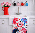 A white kitchen sink with an eco-friendly Swedish Dala Horse linen-cotton tea towel, a red pitcher with pink flowers, and four mugs hanging above on hooks.