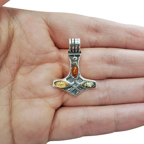 A Pendant: Multi-Color Baltic Amber Thor's Hammer, measuring 1" long by .75" wide, rests on an open palm against a white background.