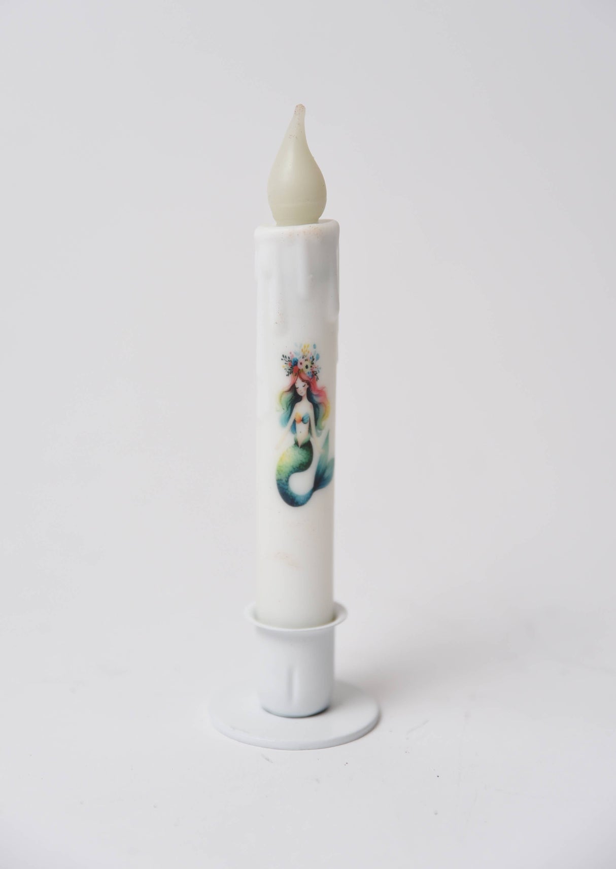 The Candle: Mermaid LED Timer Taper Candle is a white, cylinder-shaped LED candle with melted wax details and an illustrated mermaid, shown in a white holder against a plain background.