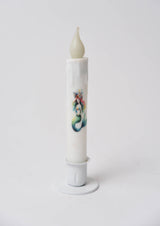 The Candle: Mermaid LED Timer Taper Candle is a white, cylinder-shaped LED candle with melted wax details and an illustrated mermaid, shown in a white holder against a plain background.