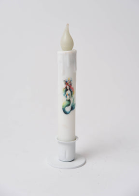 The Candle: Mermaid LED Timer Taper Candle is a white, cylinder-shaped LED candle with melted wax details and an illustrated mermaid, shown in a white holder against a plain background.