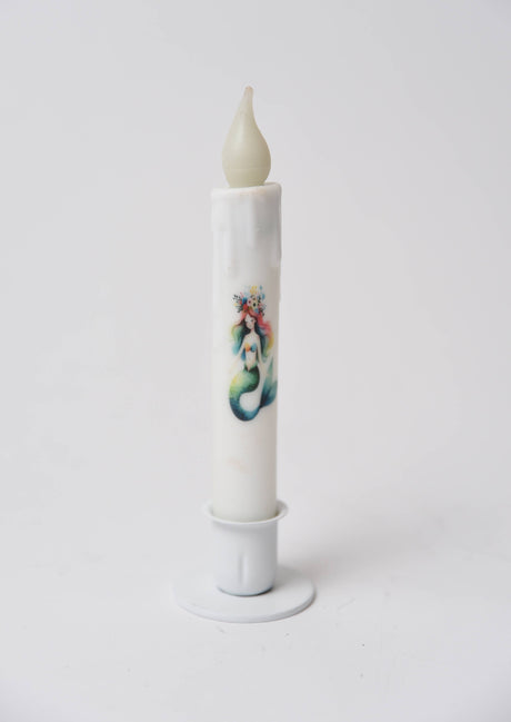 The Candle: Mermaid LED Timer Taper Candle is a white, cylinder-shaped LED candle with melted wax details and an illustrated mermaid, shown in a white holder against a plain background.