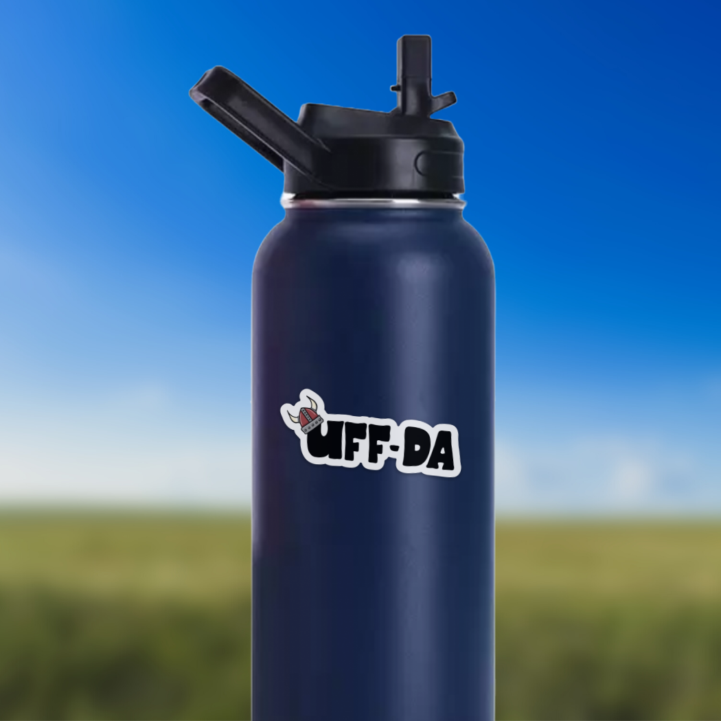 A vinyl Uff-Da sticker adorns a durable dark blue water bottle equipped with a flip straw lid, all set against the backdrop of a blurred landscape and a clear blue sky.