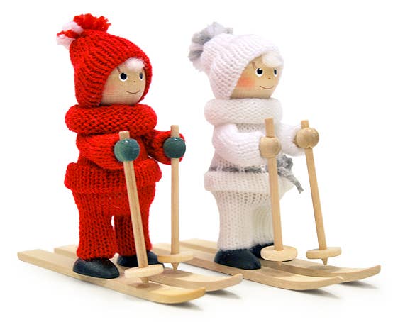 The "Figurine: Girl on Skis White" features a handmade wooden girl figurine skiing on small wooden skis with poles, dressed in charming knitted red and white attire. This decorative piece makes an ideal addition to your Christmas tree, infusing a whimsical Scandinavian touch into your festive decor.