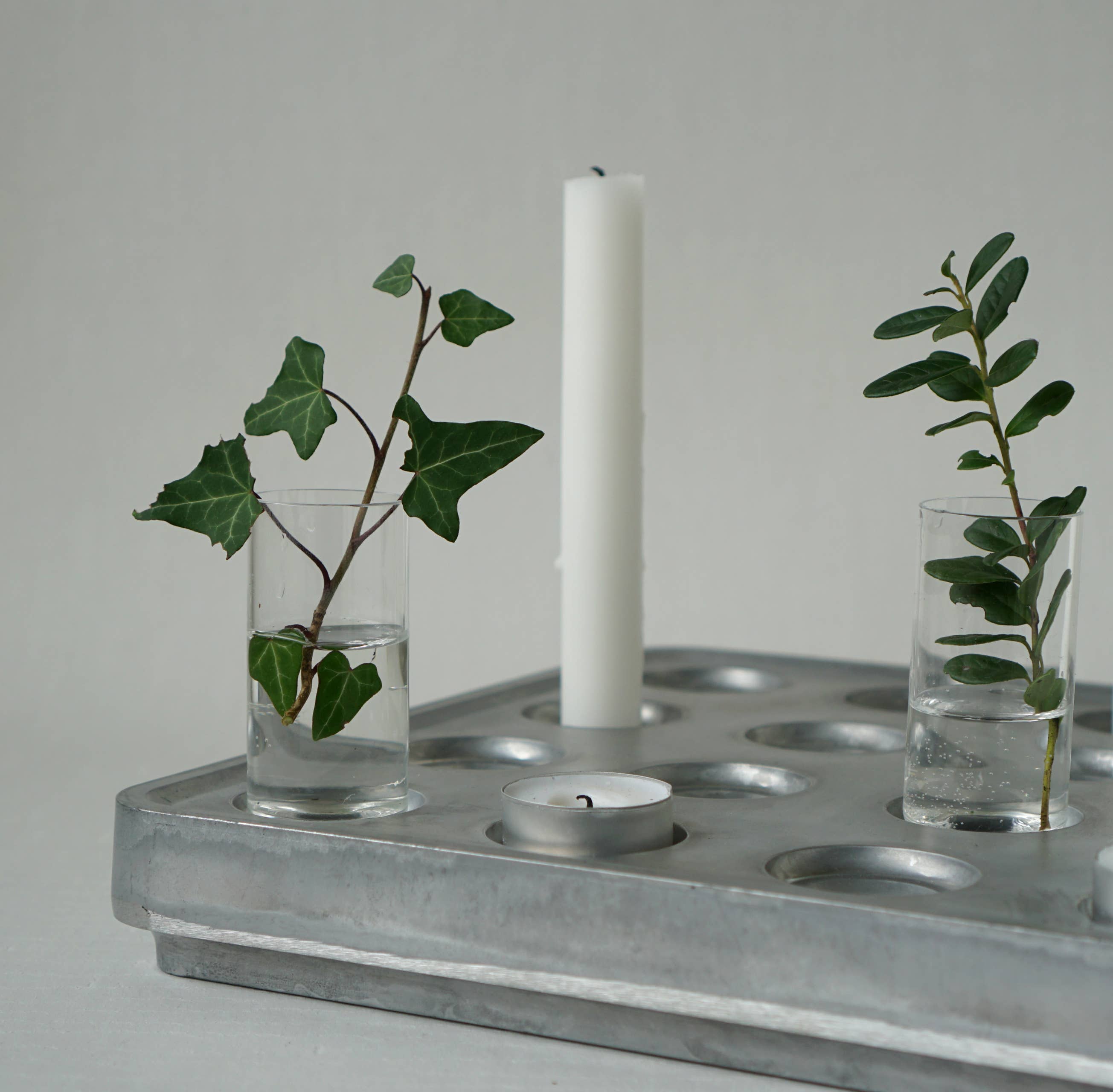 Metal tray displaying mini vases filled with greenery in glass cups, complemented by a white candle in Stumpastaken Candle Holders: Mini Vases Pack of 4, and a small tealight candle for added charm.