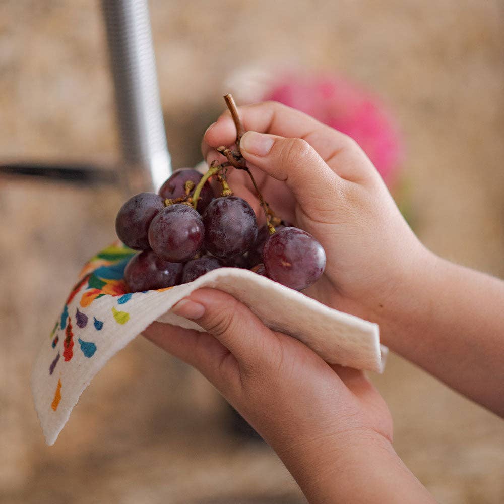 Hands holding a bunch of red grapes with a vibrant "Go Jump in the Lake" Swedish dish cloth underneath.