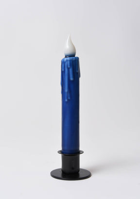 A 7" Navy Blue LED Timer Taper Candle with a white flame-shaped top stands upright in a black holder against a plain white background.