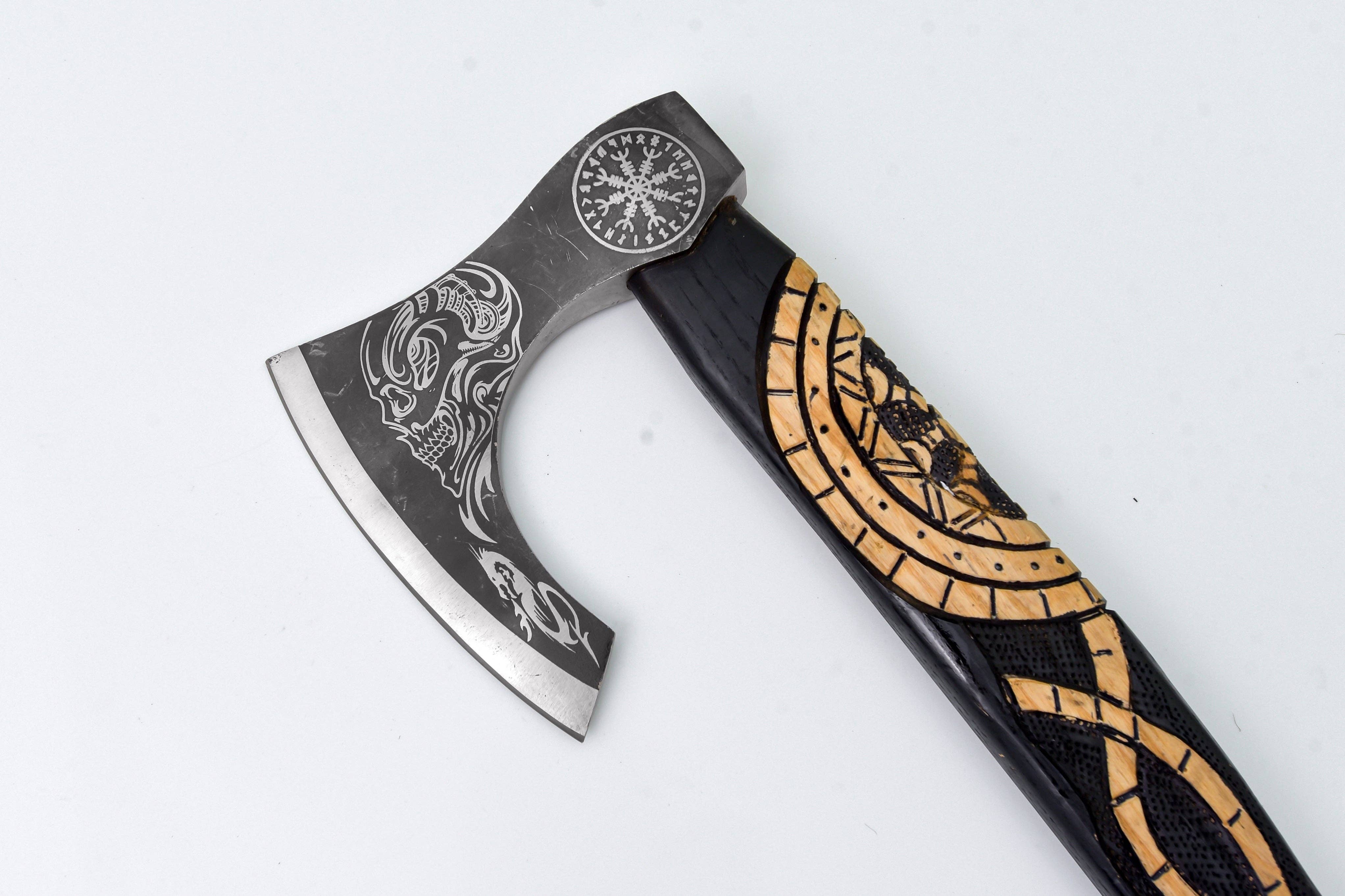 The Axe: Jörmungandr’s Grasp Camping Tool features an engraved carbon steel blade and a black and gold handle with ornate carvings inspired by Norse symbology, shown against a white background.